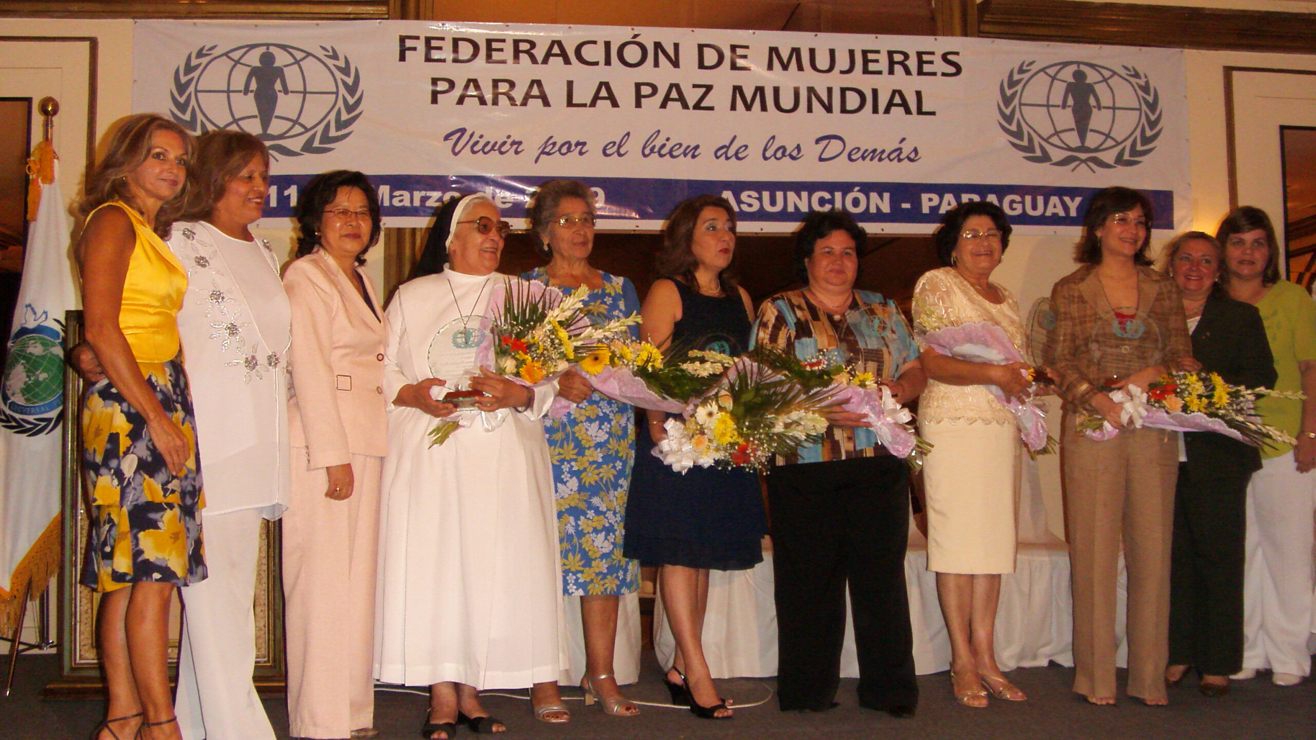 A group of women posing for a picture at a Primera Edición ceremony, showcasing their commitment to Vivir por el bien de los Demás.