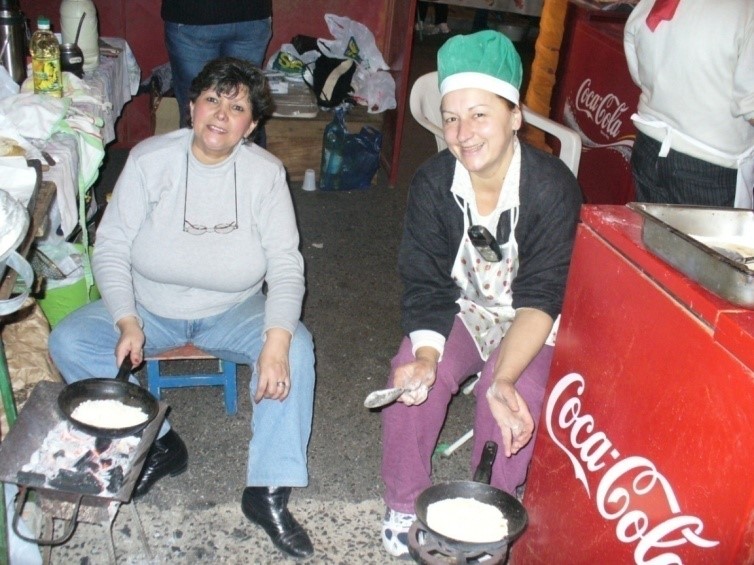 Two women cooking food on a stove in front of a Coca Cola, near San Juan.