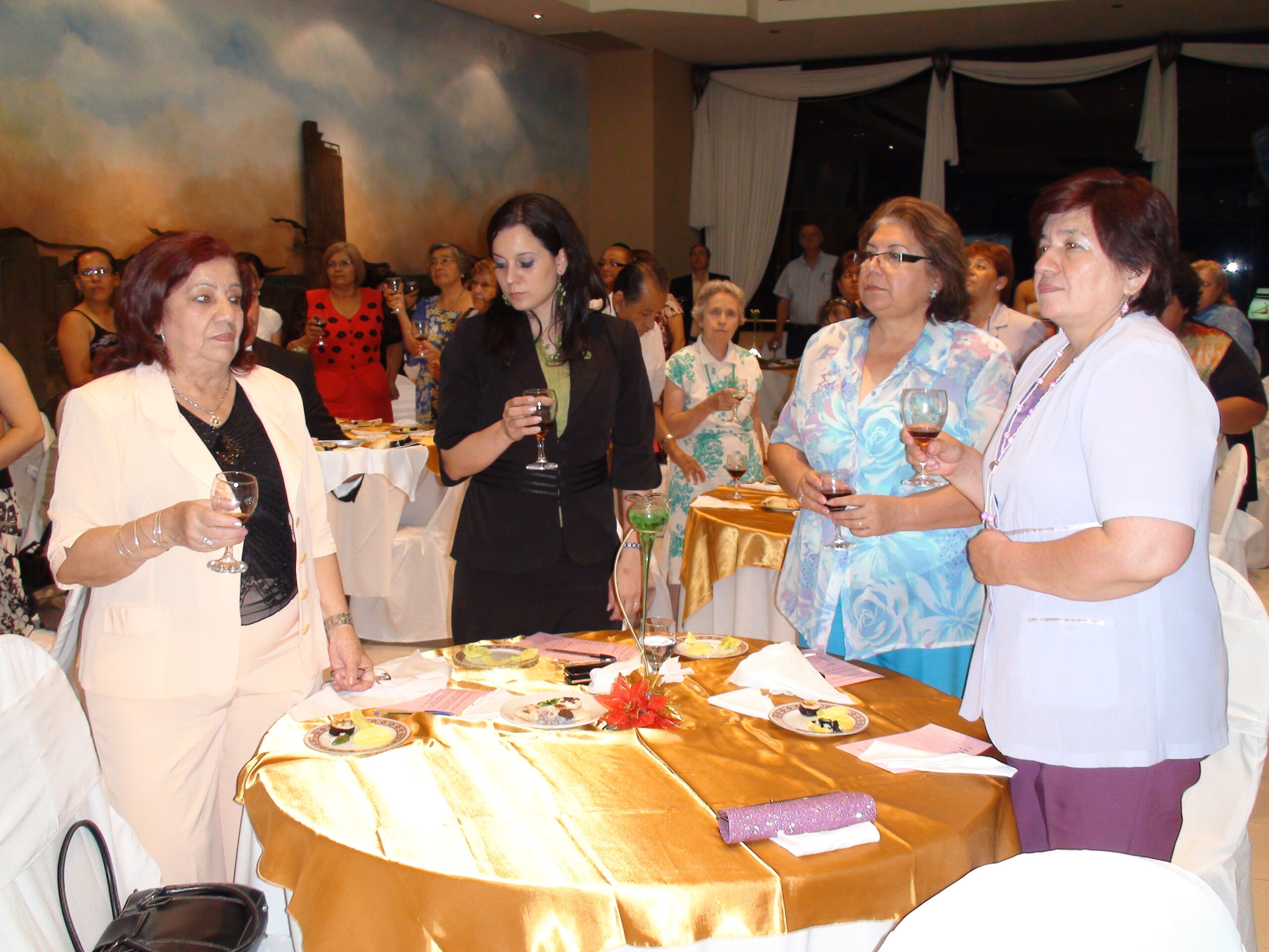 A group of women standing around a table during the Área Mujer's brindis event, celebrating the cierre de actividades.