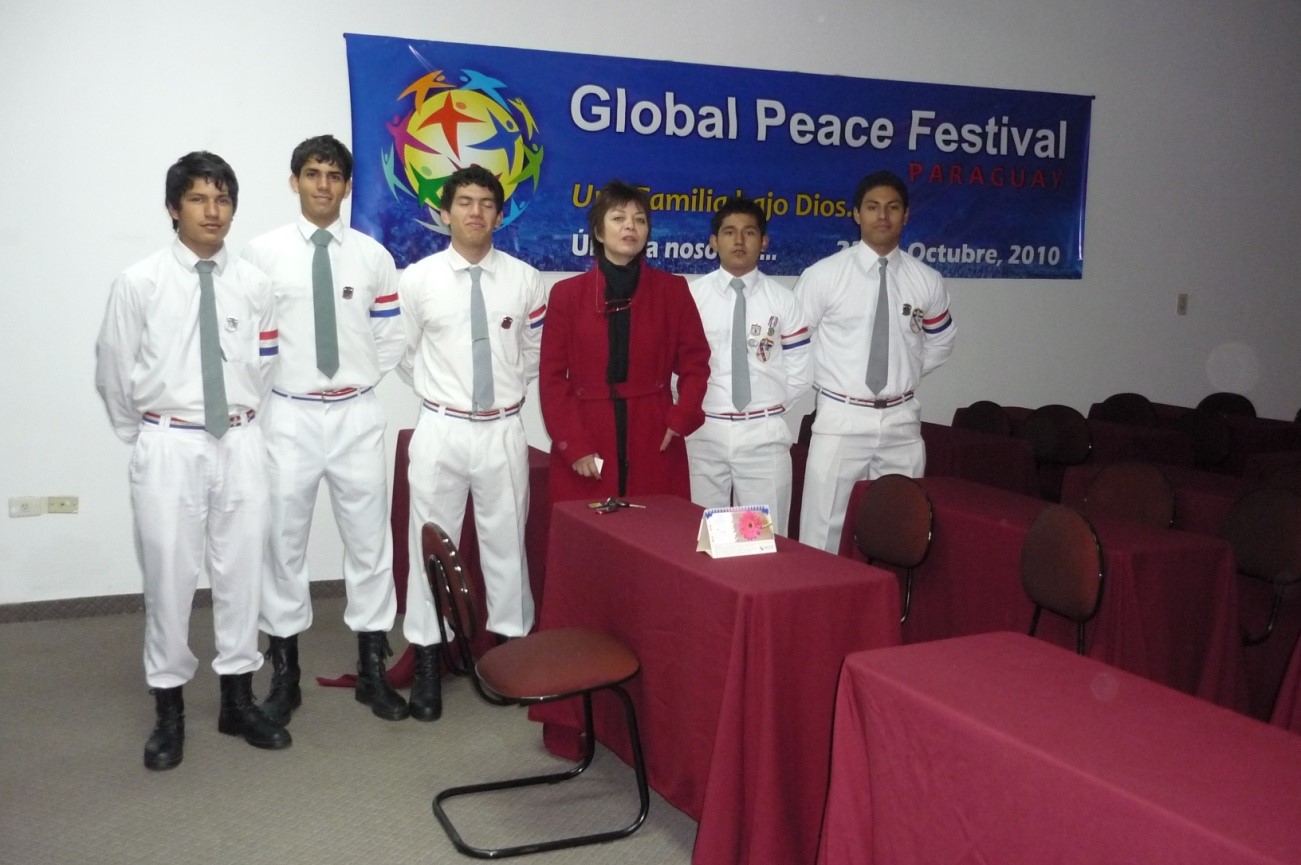 Un grupo de estudiantes frente a un banner que dice Visita al festival de paz global.