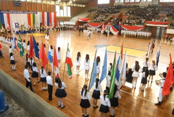 A group of people standing on a gymnasium floor with flags, participating in the JUEGOS GLOBALES.