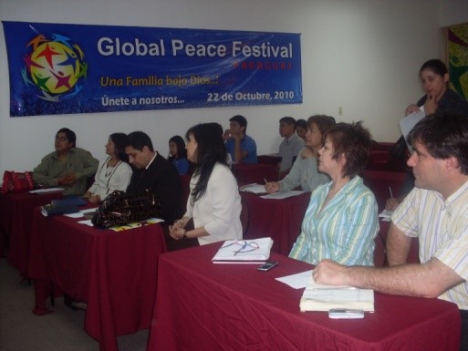 Un grupo de personas sentadas en una mesa frente a una pancarta que dice Juegos Globales de la Paz.