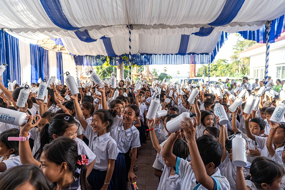 A group of school children in Cambodia are holding up white cups as part of an education project funded by Projects for Peace.