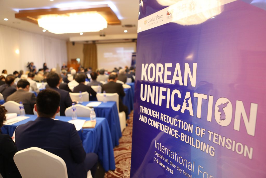A sign reading Korean Unification in a conference room full of participants