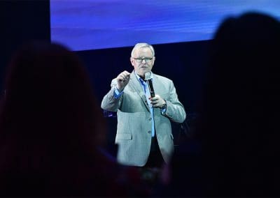 A man in a suit speaking at a podium with a microphone in front of an audience.