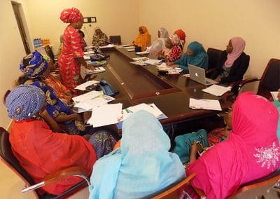 Women in traditional attire participating in a meeting around a conference table.