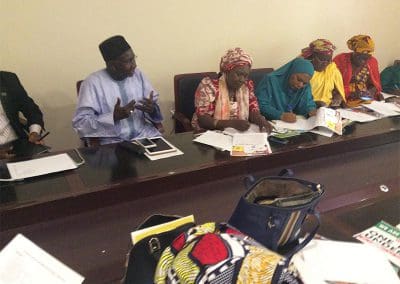 Group of individuals engaged in a meeting with papers and electronic devices on the table.