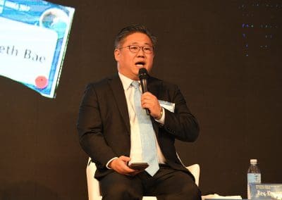 A man seated, speaking into a microphone at an event.