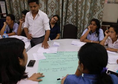 A person presenting ideas to a group at a meeting with notes and a budget plan visible on the table.