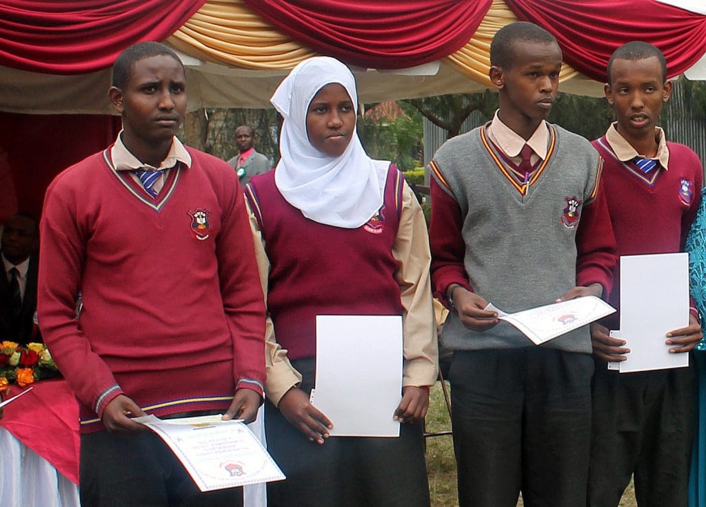 A group of young people holding papers in front of a red curtain.