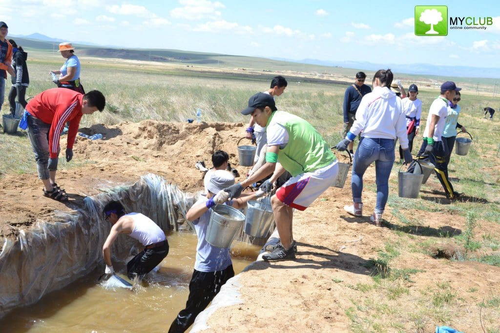 Group of volunteers cleaning and maintaining a water reservoir in a grassland area.