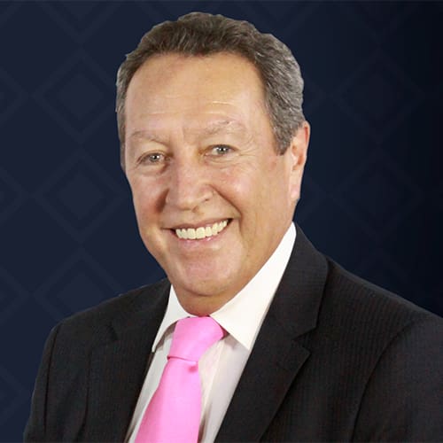 A smiling man in a suit, featuring a bright pink tie, stands confidently against a dark patterned background. This striking image captures the charismatic presence akin to that of Marco Vinicio Cerezo.