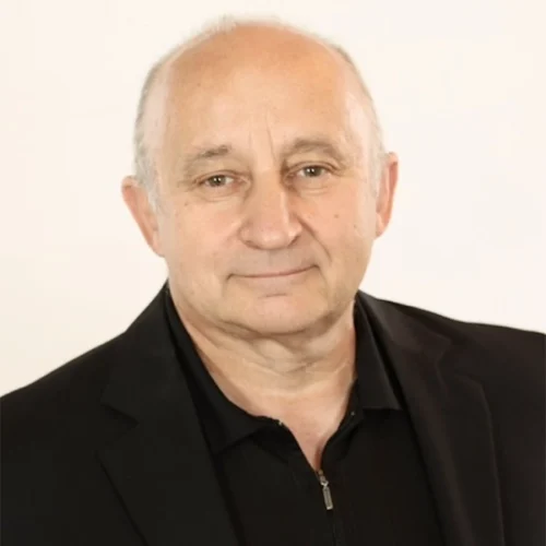 Rev. Mark Farr, a middle-aged man with short, thinning hair, wears a black jacket and black shirt as he faces the camera against a plain light background.