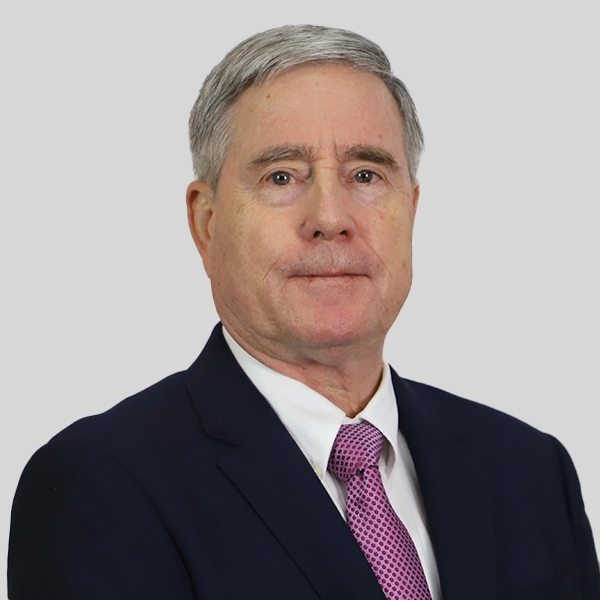 Thomas Field, a man with gray hair wearing a dark suit, white shirt, and pink patterned tie, poses against a plain light gray background.
