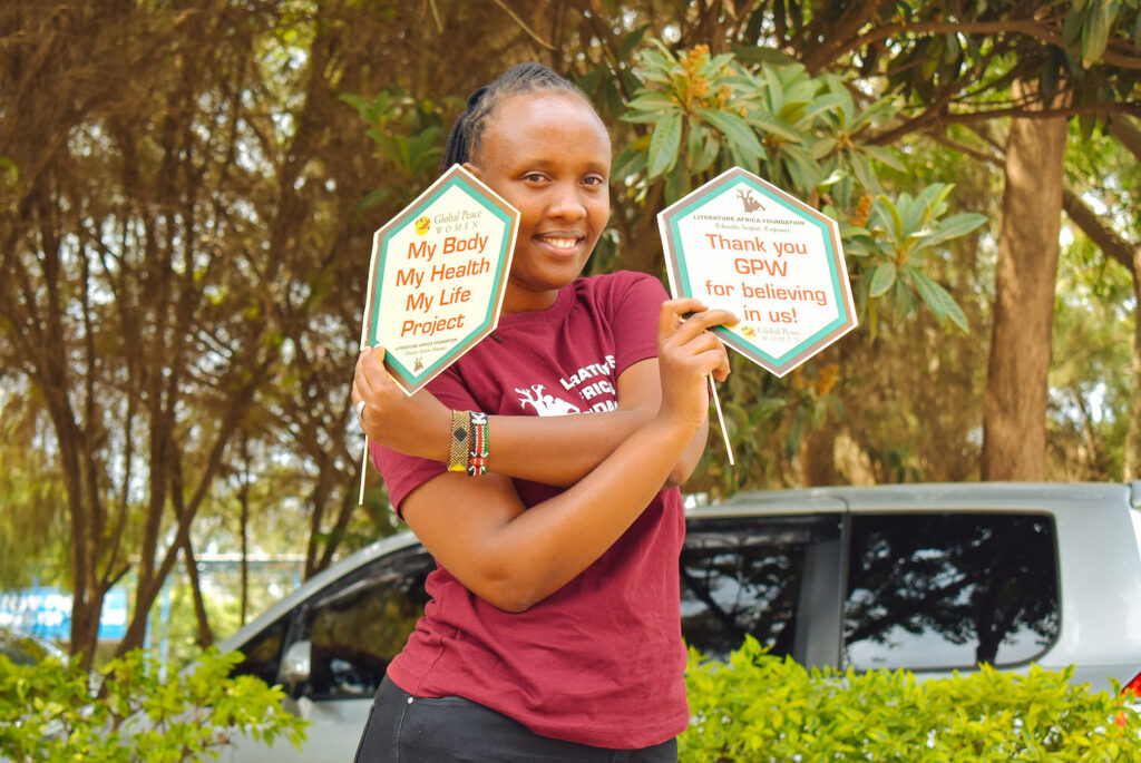 Wairimu Mwangi, a young woman, hold signs reading 'My Body, My Health, My Life Project' and 'Thank you GPW for believing in us'