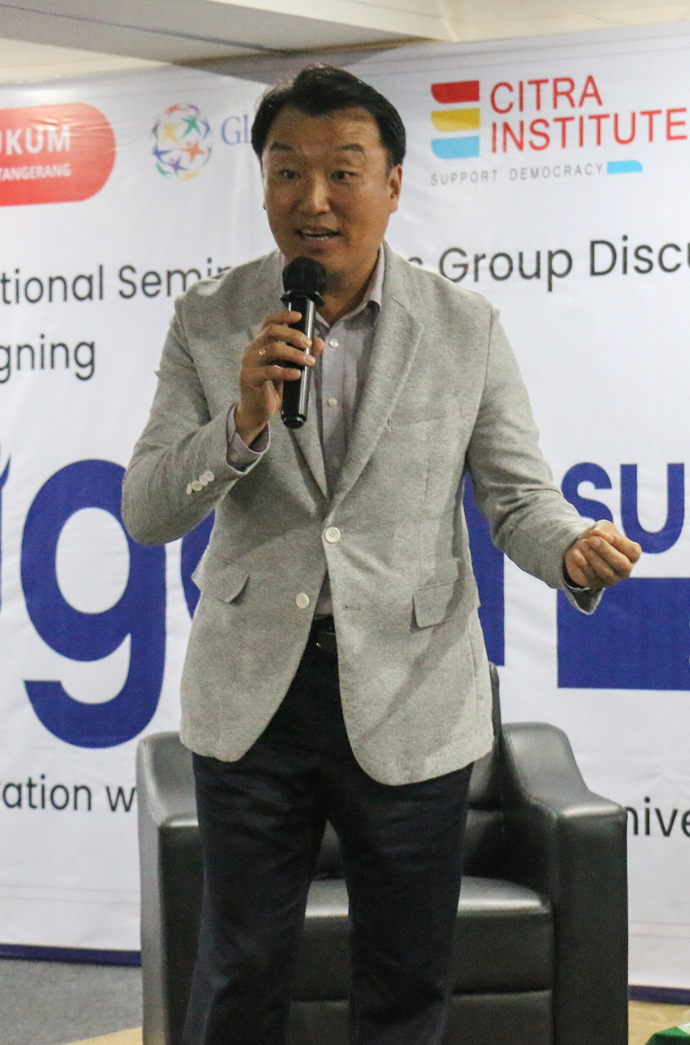 A man in a suit speaking into a microphone at GPF Indonesia's UGen Seminar highlighting Pancasila and Global Peace.