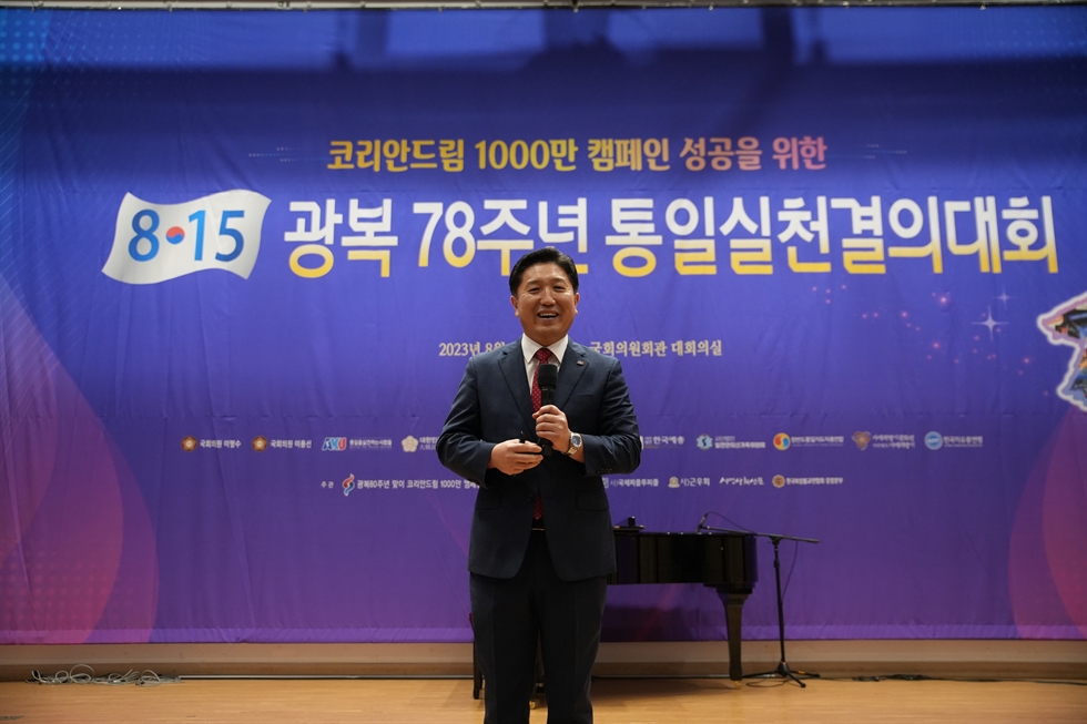 A man in a suit speaking on stage at the Korean Unification Campaign launch at the National Assembly.