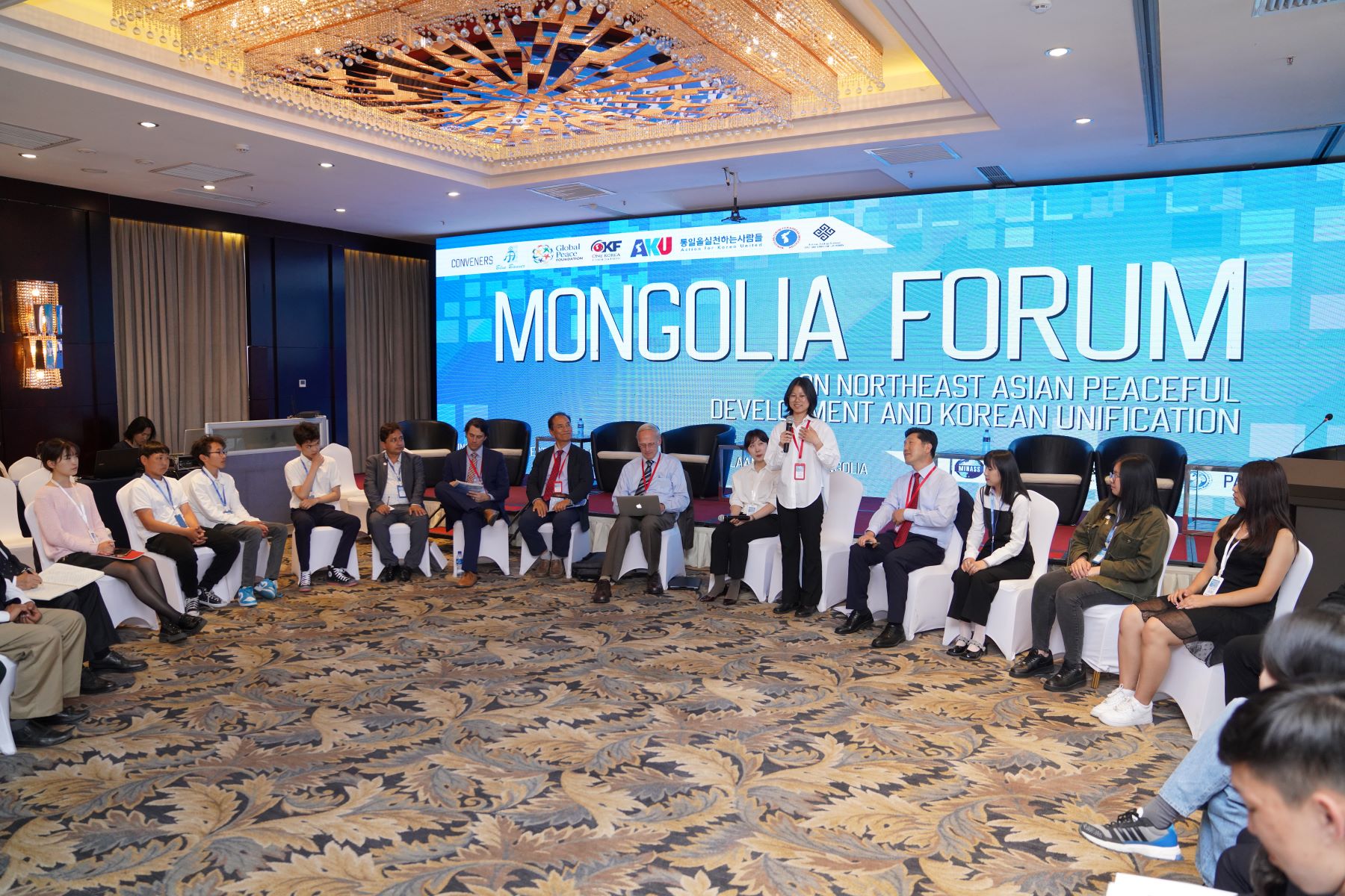 A group of people from Mongolia sitting around a table in front of a large screen.
