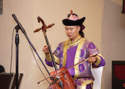 A man, representing Mongolia, gracefully plays a cello in front of a microphone - showcasing their unique role in peacebuilding.