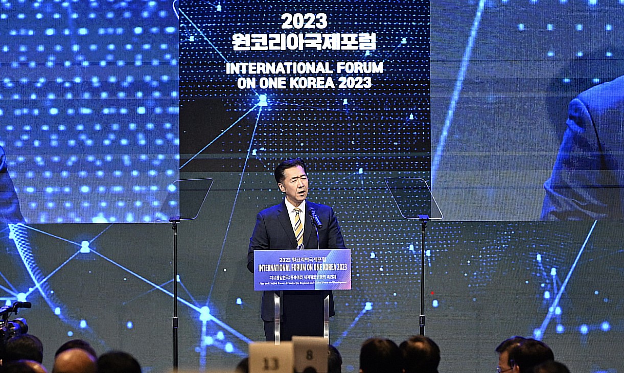 A man speaking at a podium in front of a large screen at the International Forum on One Korea discussing peace and security.