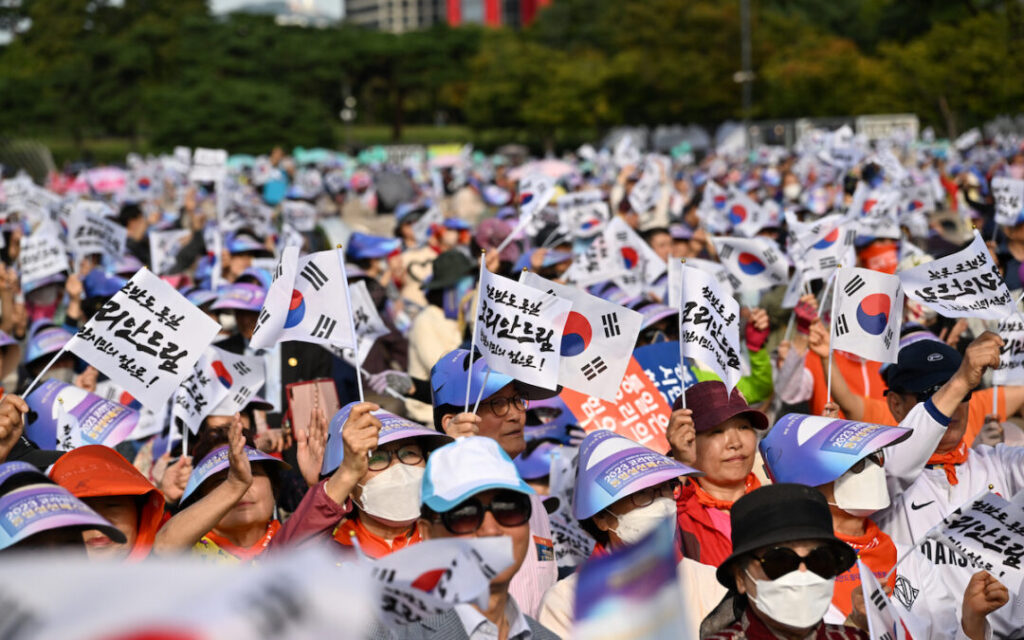 Over 20 citizens holding signs with Korean flags, participating in the grassroots unification movement for global peace.
