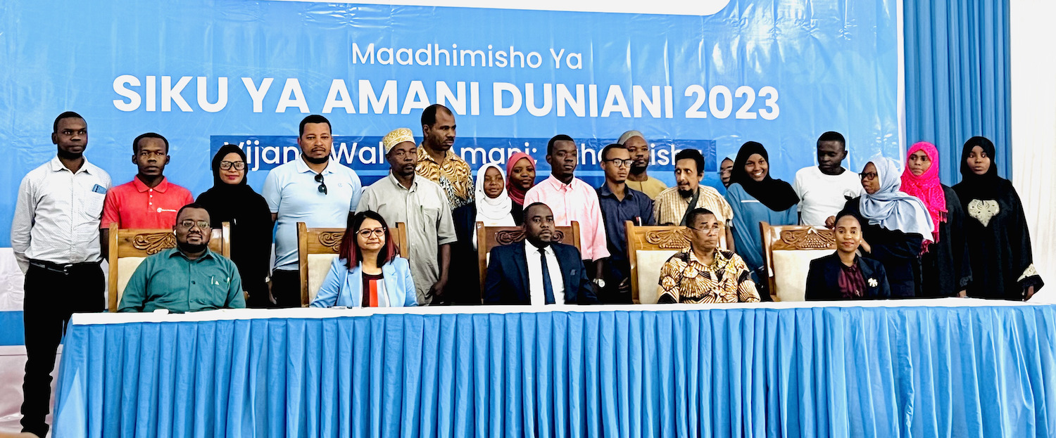 A group of people from Tanzania gathered in front of a blue table to celebrate International Day of Peace 2023.