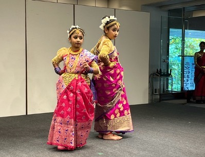 Two girls from different cultures wearing traditional Indian saris standing on stage at a multicultural family festival.