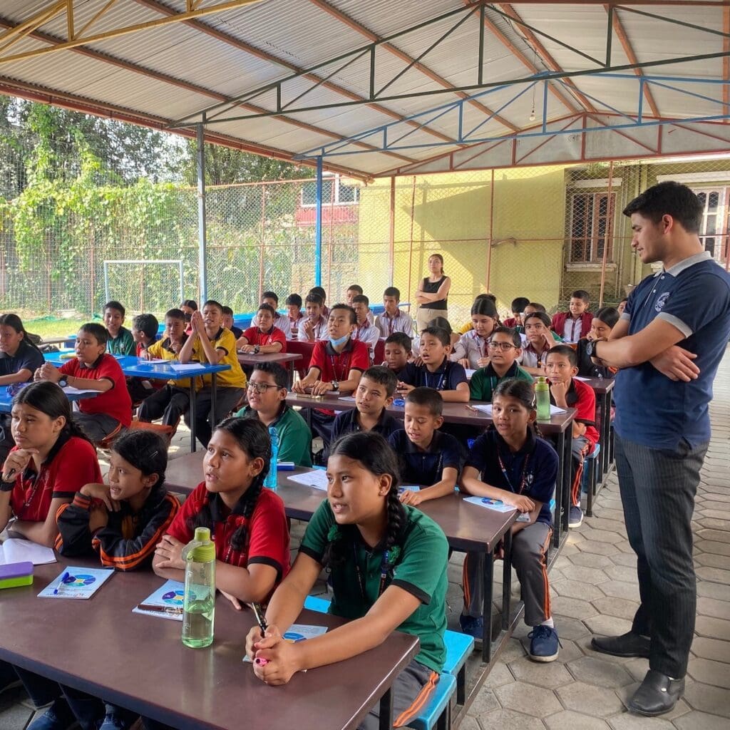 A group of children are sitting at desks in a classroom in Nepal, engaging in peacebuilding training.