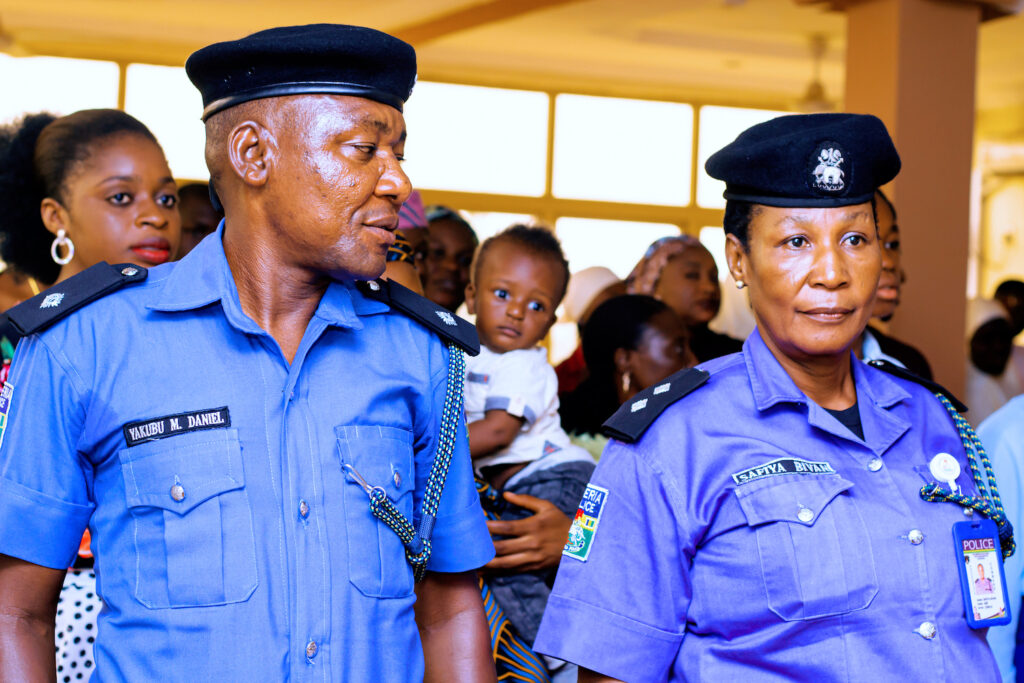 Two police officers standing next to a group of people celebrating International Day of Nonviolence in Kaduna, Nigeria.