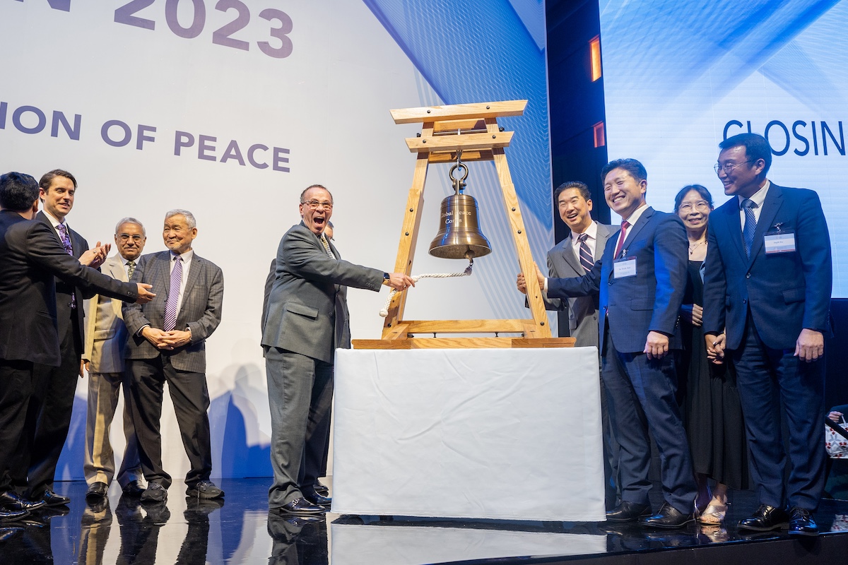 A group of people standing next to a bell on a Global Peace Convention stage.