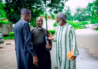 Three men engaging in a conversation in front of a building in Nigeria, contributing to the deepening democracy efforts.