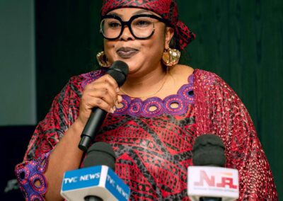 In Nigeria, a woman wearing a striking red dress passionately speaks into a microphone, contributing to the deepening democracy in the country.