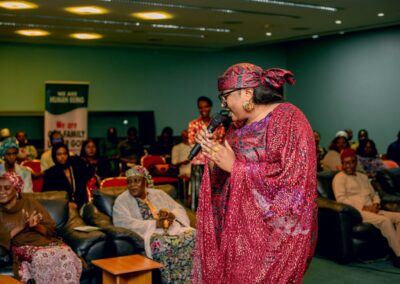 A woman in a red dress standing in front of an audience, promoting Deepening Democracy in Nigeria.
