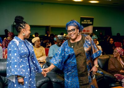 Two women shaking hands in front of an audience during a Deepening Democracy conference in Nigeria.