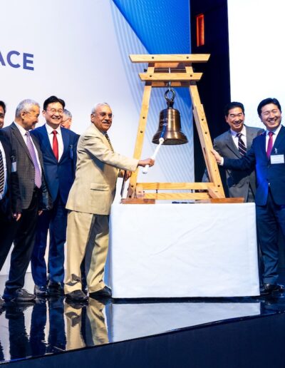 A group of men and women standing next to a wooden bell at the Global Peace Convention.