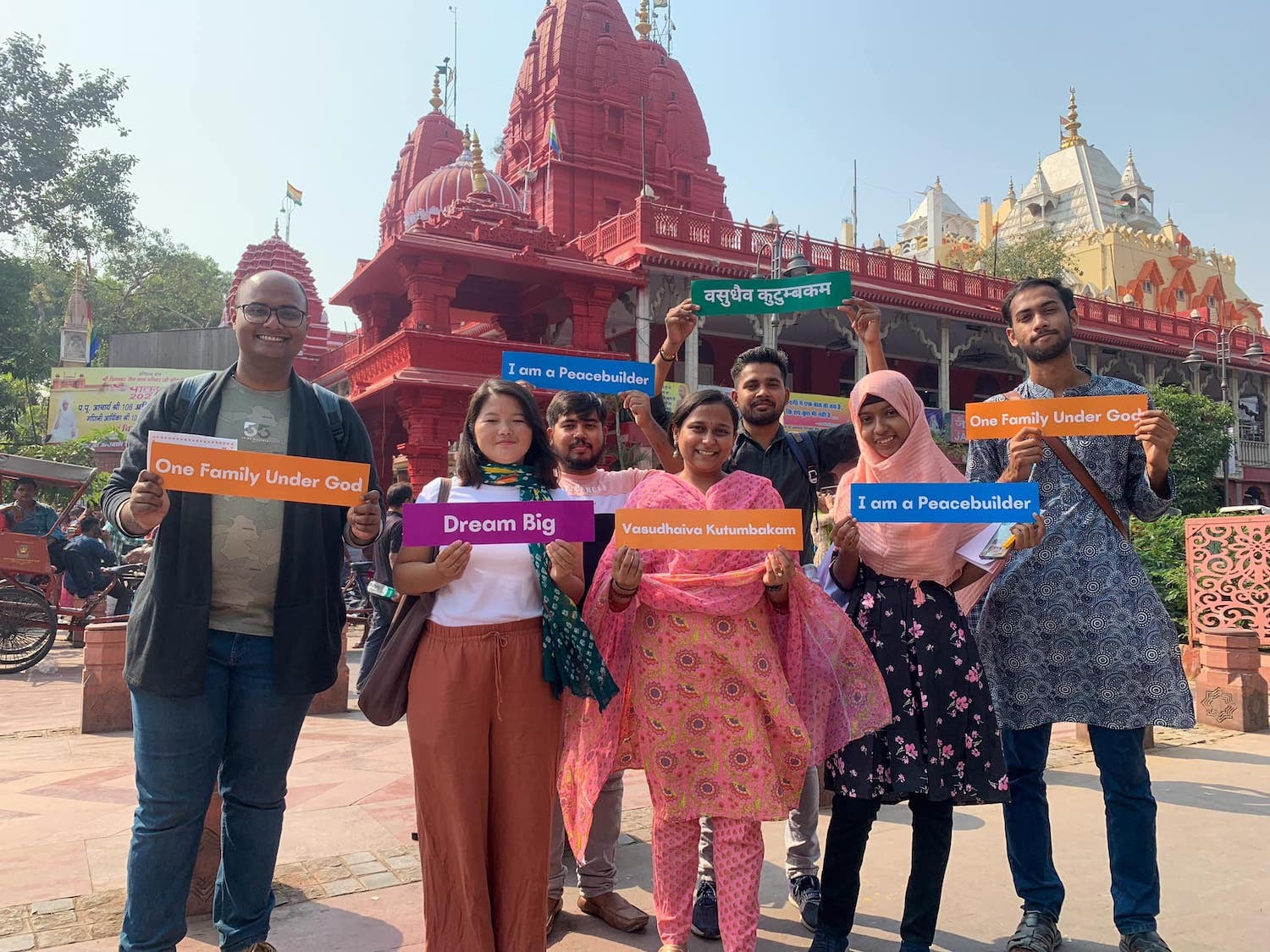 A group of people promoting interfaith leadership by holding signs in front of a temple.