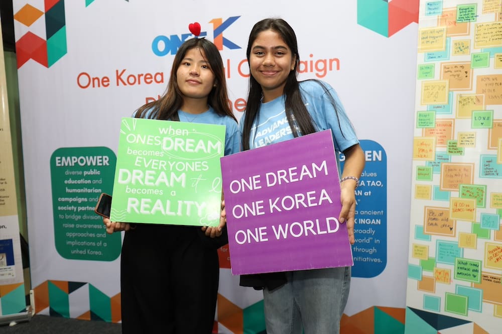 Two students holding signs at the global peace youth festival, expressing one dream and one reality.