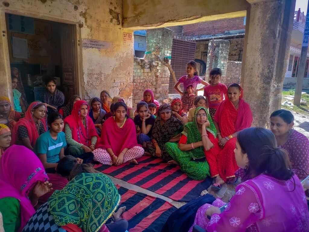 As part of a Period Awareness Drive in India, a group of empowered women in pink saris gather together, sitting on the ground.