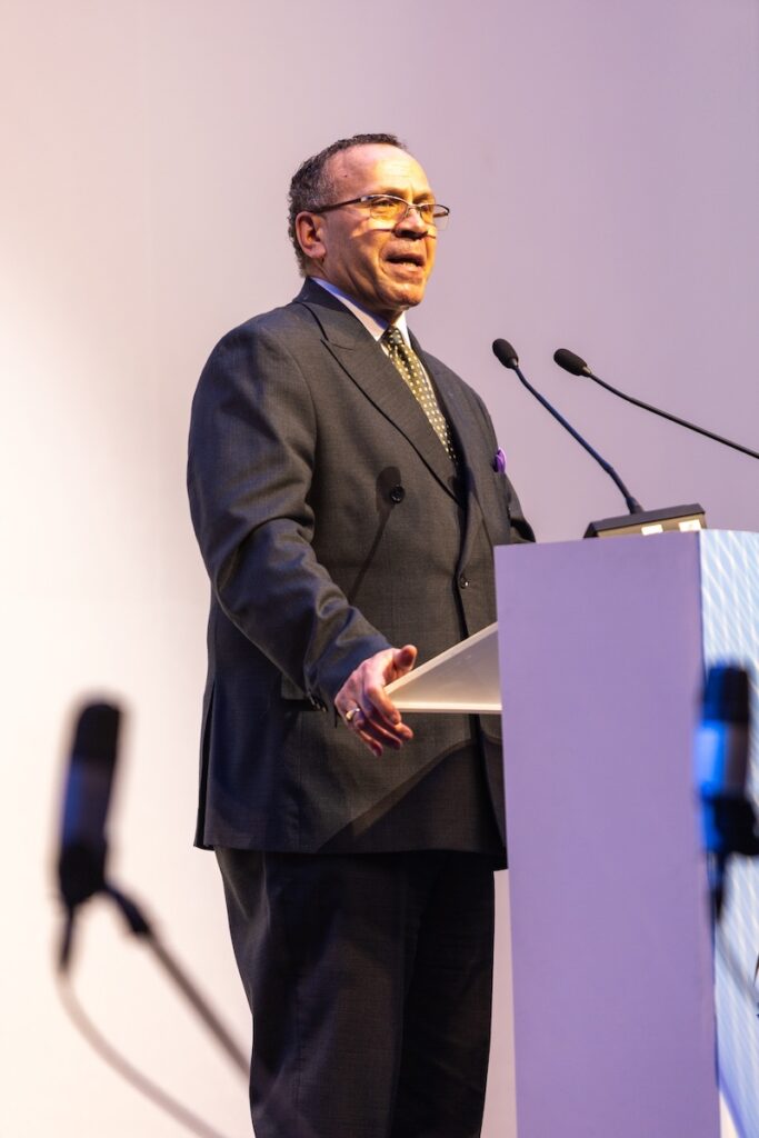 A man in a suit standing at a podium, addressing the Global Peace Convention.