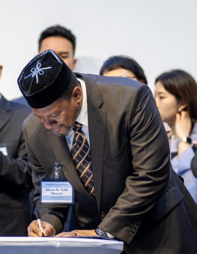 A man signing a document at the Global Peace Convention, with a group of people witnessing the momentous occasion.