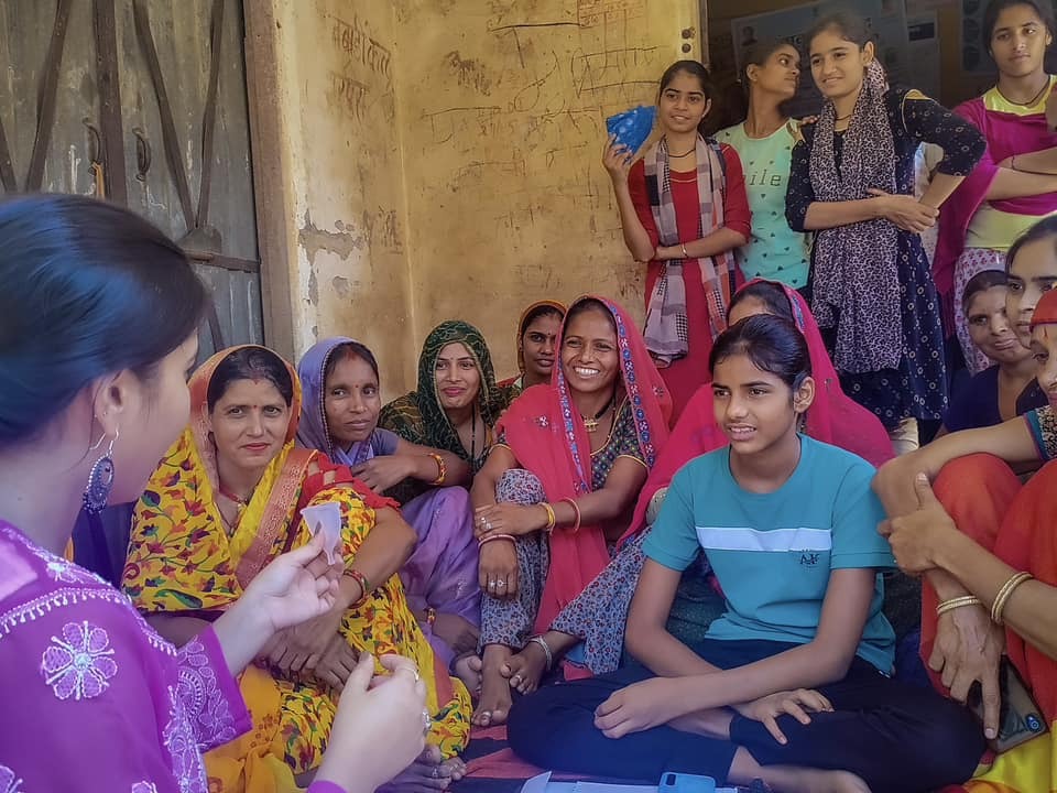 A group of women in saris sitting on the ground, creating awareness about period hygiene.