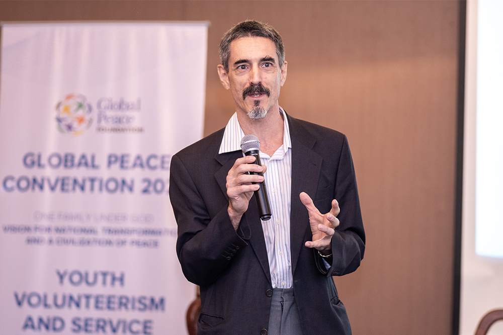 An engaging man giving a speech at the global peace convention, inspiring young people in peacebuilding.