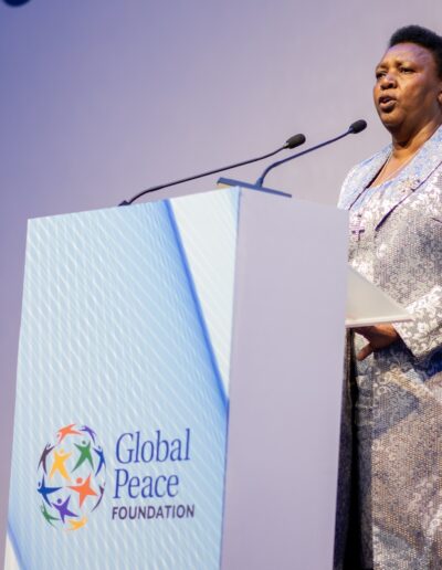 A woman giving a speech at the Global Peace Convention, standing confidently behind a podium.