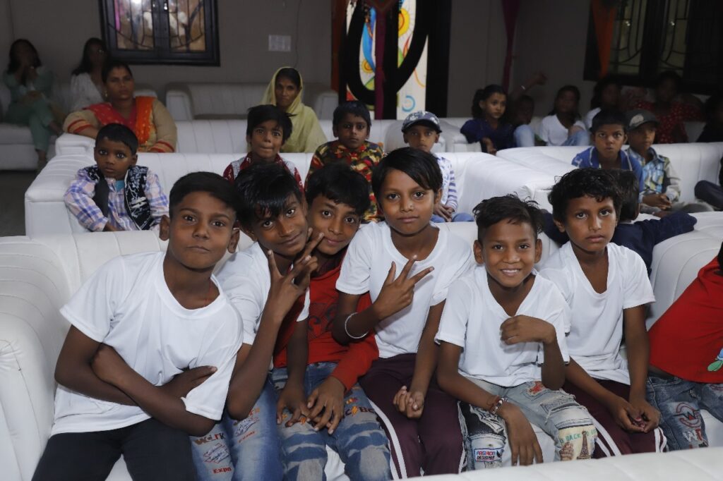 A group of children posing for a picture in front of a white couch during S.M.I.L.E Annual Day.