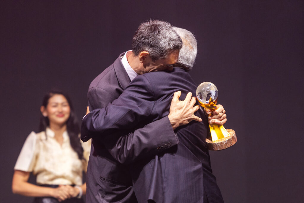 Two men embracing each other with joy on stage during the Awards Gala at the 2023 Global Peace Convention.