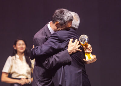 Two men embracing each other with joy on stage during the Awards Gala at the 2023 Global Peace Convention.