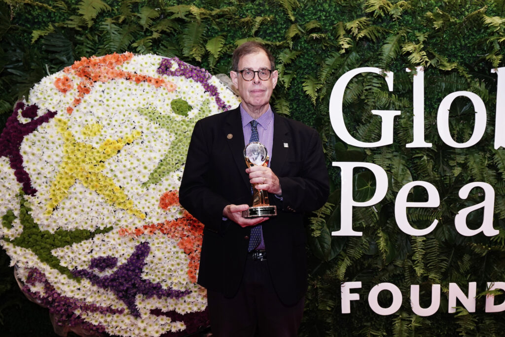 A man in a suit standing in front of a flower wall at the Global Peace Convention.