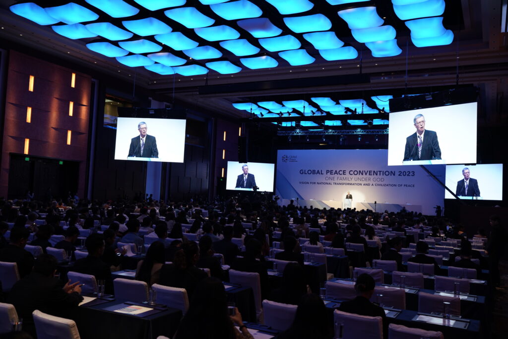 A Community-Driven Peacebuilding gathering in 2023, featuring an International Convening in a large room full of people watching a large screen at the Global Peace Convention.
