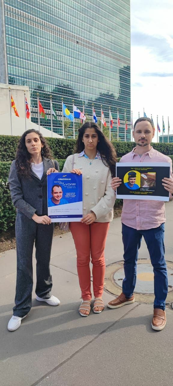 Three people holding up signs in front of the UN building to raise awareness about GPF Brazil.