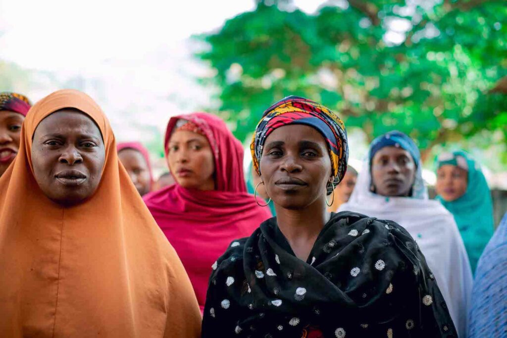 A group of women in colorful headscarves standing next to each other, representing the Economic Empowerment achieved through Women's Cooperative Societies, like GPF Nigeria.